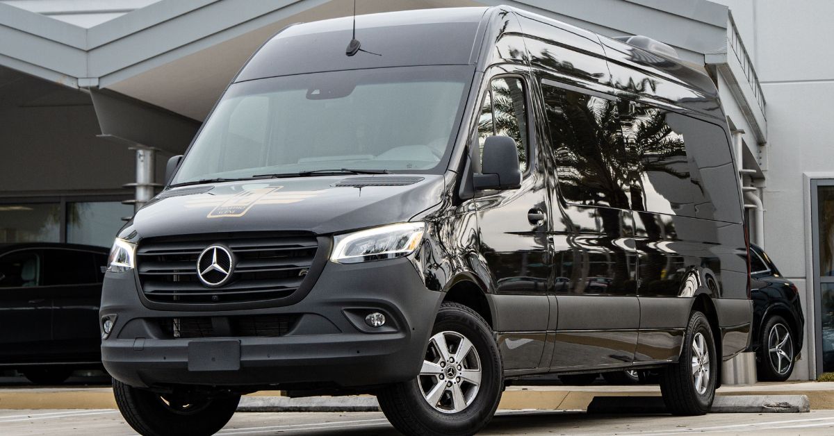 Black Mercedes-Benz Sprinter passenger van parked outside a modern building, featuring a high roof, spacious cabin, and premium shuttle design.