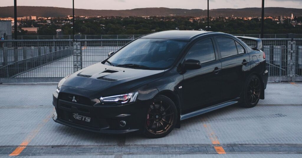 Black Mitsubishi Lancer Evolution sedan parked on a rooftop, featuring sporty styling, black alloy wheels, and an aggressive performance design.
