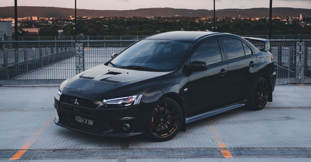 Black Mitsubishi Lancer Evolution sedan parked on a rooftop, featuring sporty styling, black alloy wheels, and an aggressive performance design.
