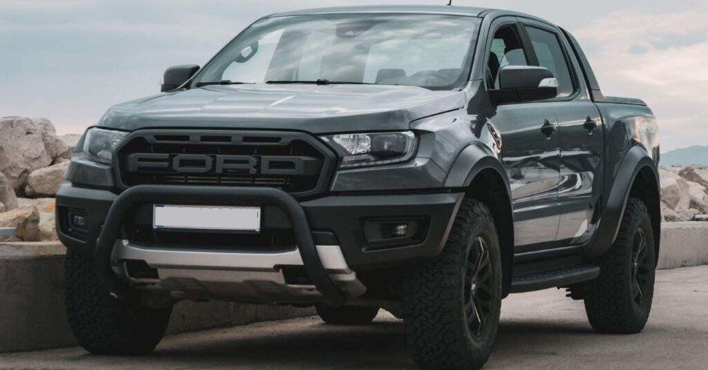 Gray Ford Ranger pickup truck parked by a waterfront, featuring rugged styling, off-road tires, and a bold front grille.
