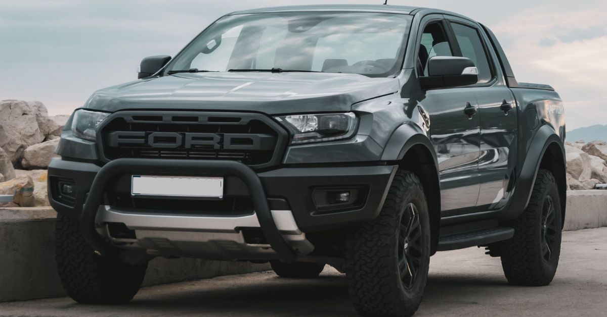 Gray Ford Ranger pickup truck parked by a waterfront, featuring rugged styling, off-road tires, and a bold front grille.