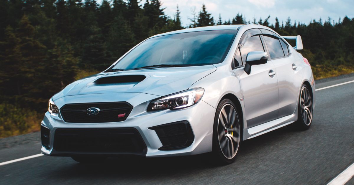 Silver Subaru WRX STI sedan driving on a highway, featuring sporty styling, LED headlights, a hood scoop, and a rear spoiler.