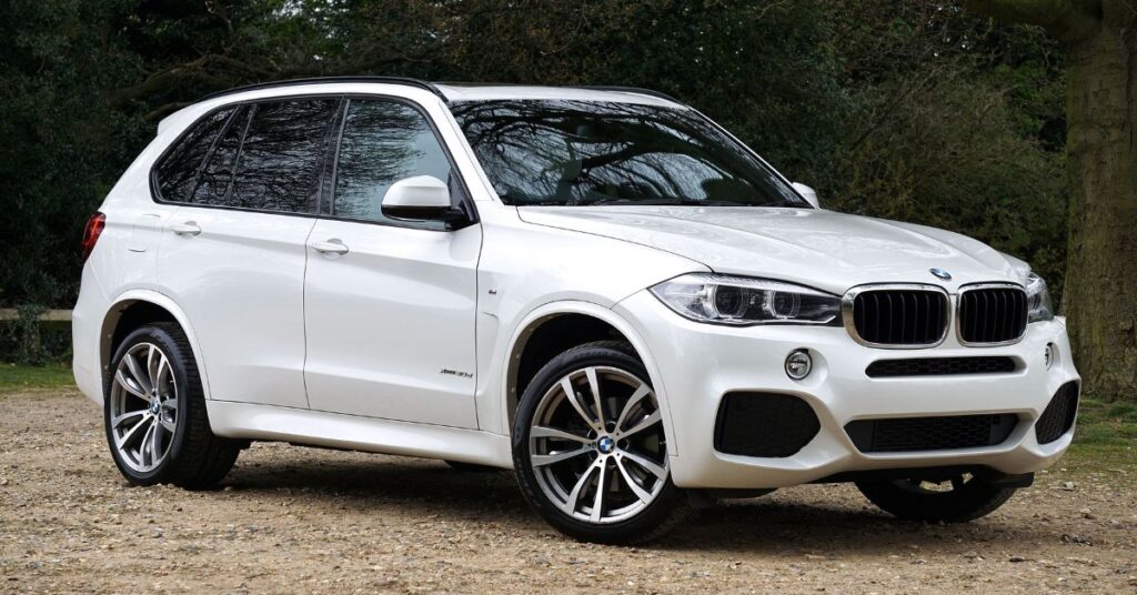White BMW X5 SUV parked on a gravel driveway, showcasing its sporty design, alloy wheels, and modern front grille.