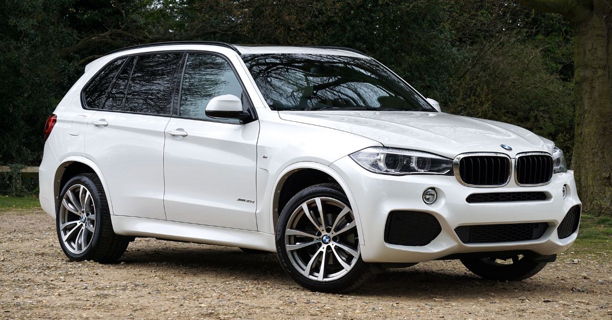 White BMW X5 SUV parked on a gravel driveway, showcasing its sporty design, alloy wheels, and modern front grille.