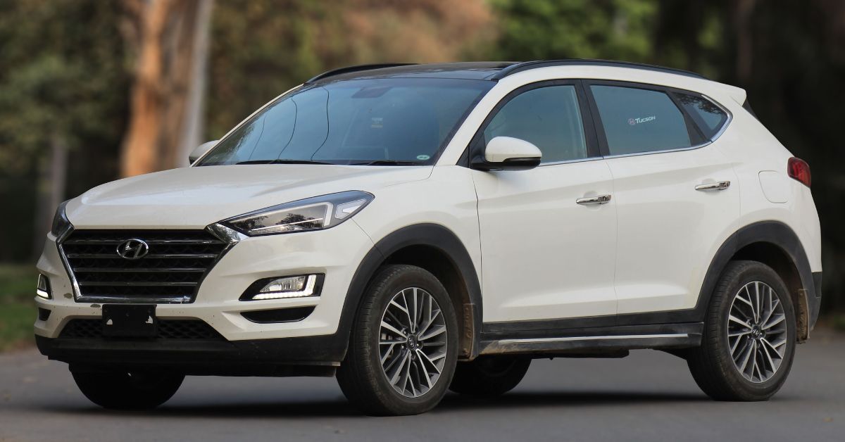 White Hyundai Tucson SUV parked on a quiet road, showcasing its modern grille, LED headlights, alloy wheels, and sleek crossover design.