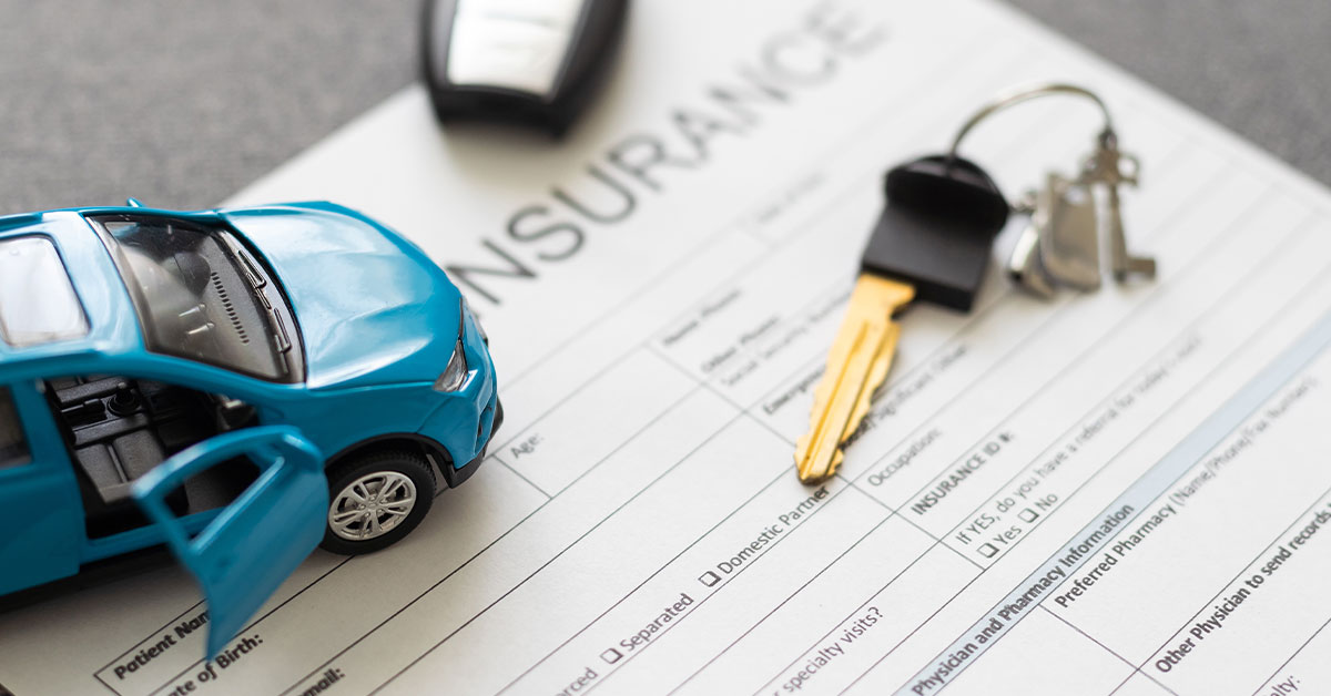 Paperwork of car insurance with car key and toy car sitting on top.
